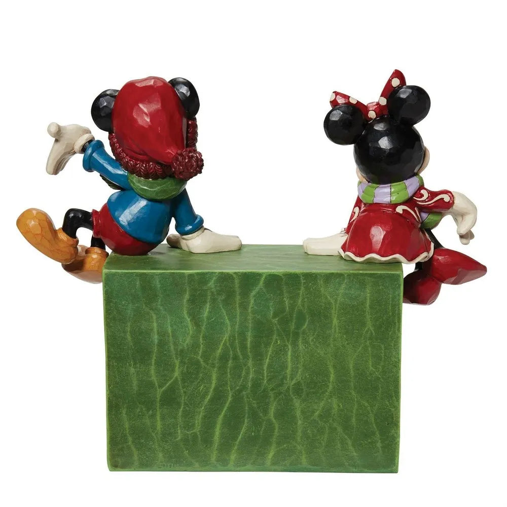 Back view of Mickey and Minnie Mouse Christmas figurines in winter outfits, perched on a green countdown block. 