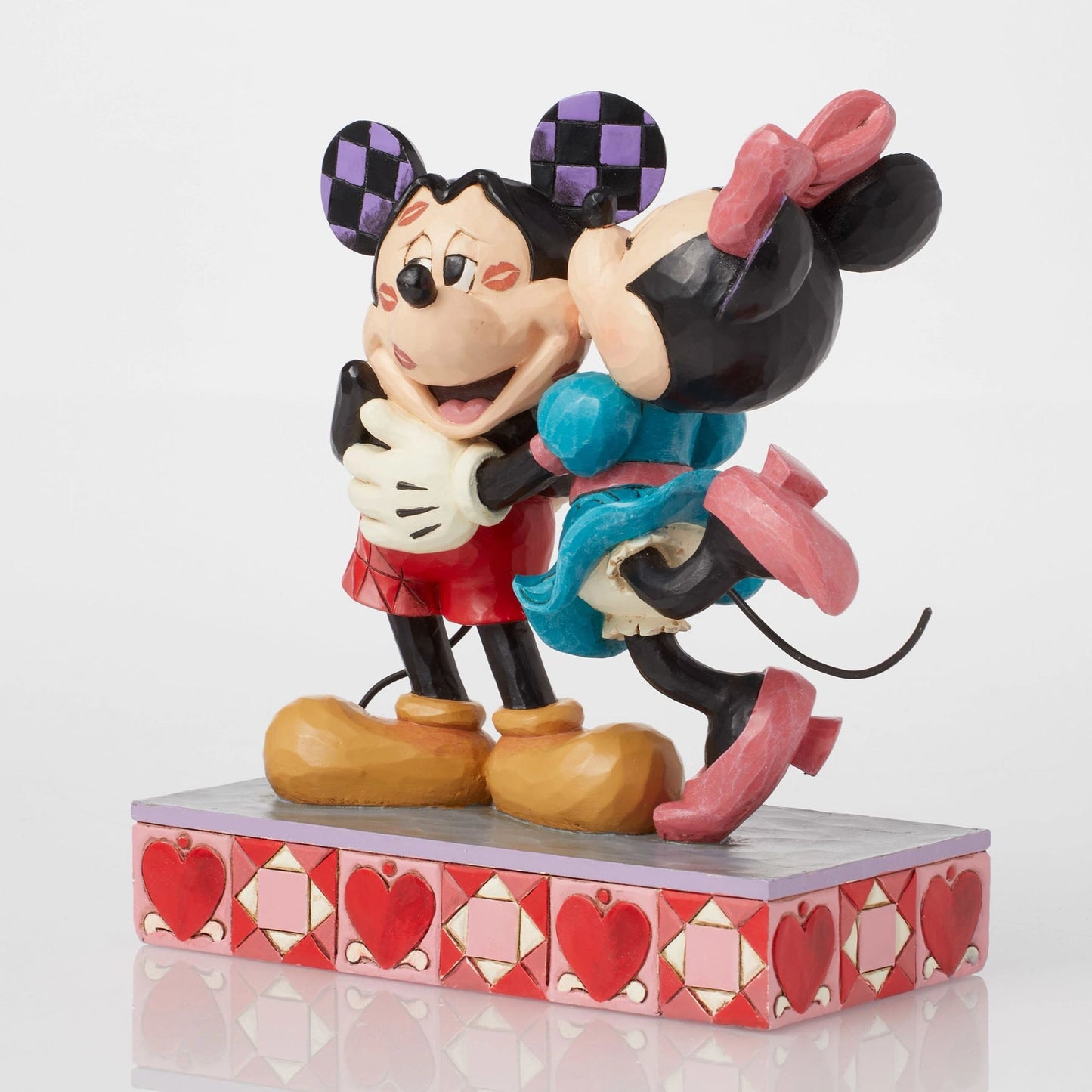Side view of Mickey and Minnie Mouse figurine embracing, red shorts and teal dress detail, heart-patterned base