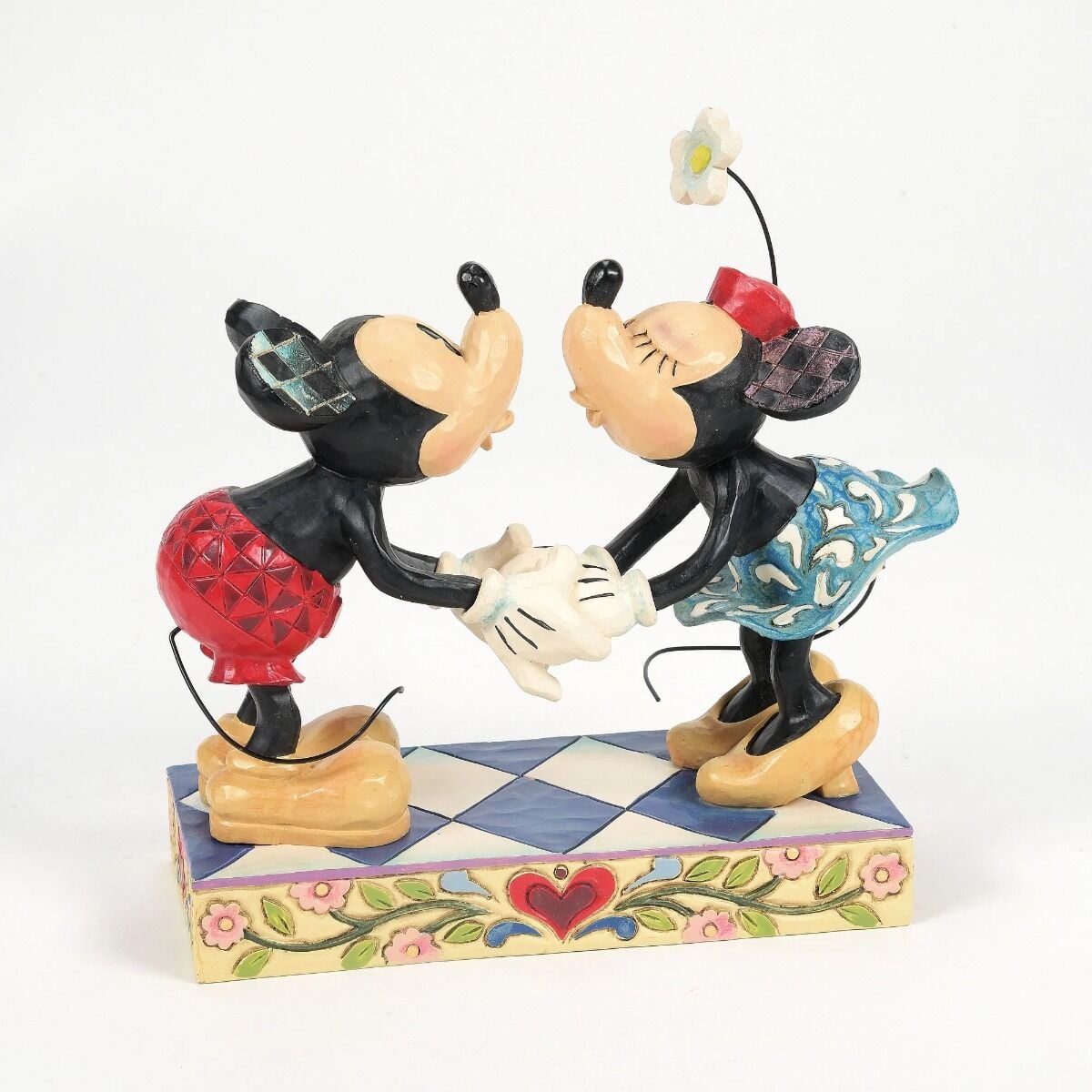 Mickey and Minnie Mouse kissing figurine front three-quarter view, hands clasped at centre, Minnie's blue skirt visible, on a floral base