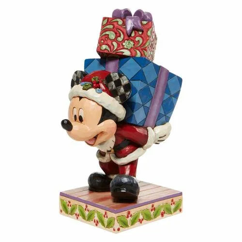 Side view of Mickey Mouse in a Santa hat figurine, leaning forward carrying a tall stack of wrapped Christmas presents. 