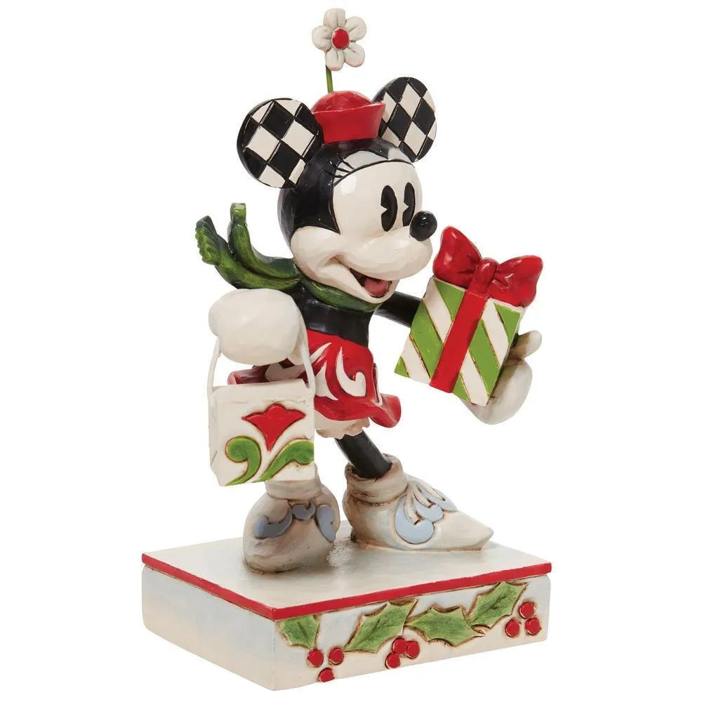 Angled front view of Minnie Mouse figurine in red scrollwork dress, checkered ears, carrying striped gift and shopping bag, holly base 