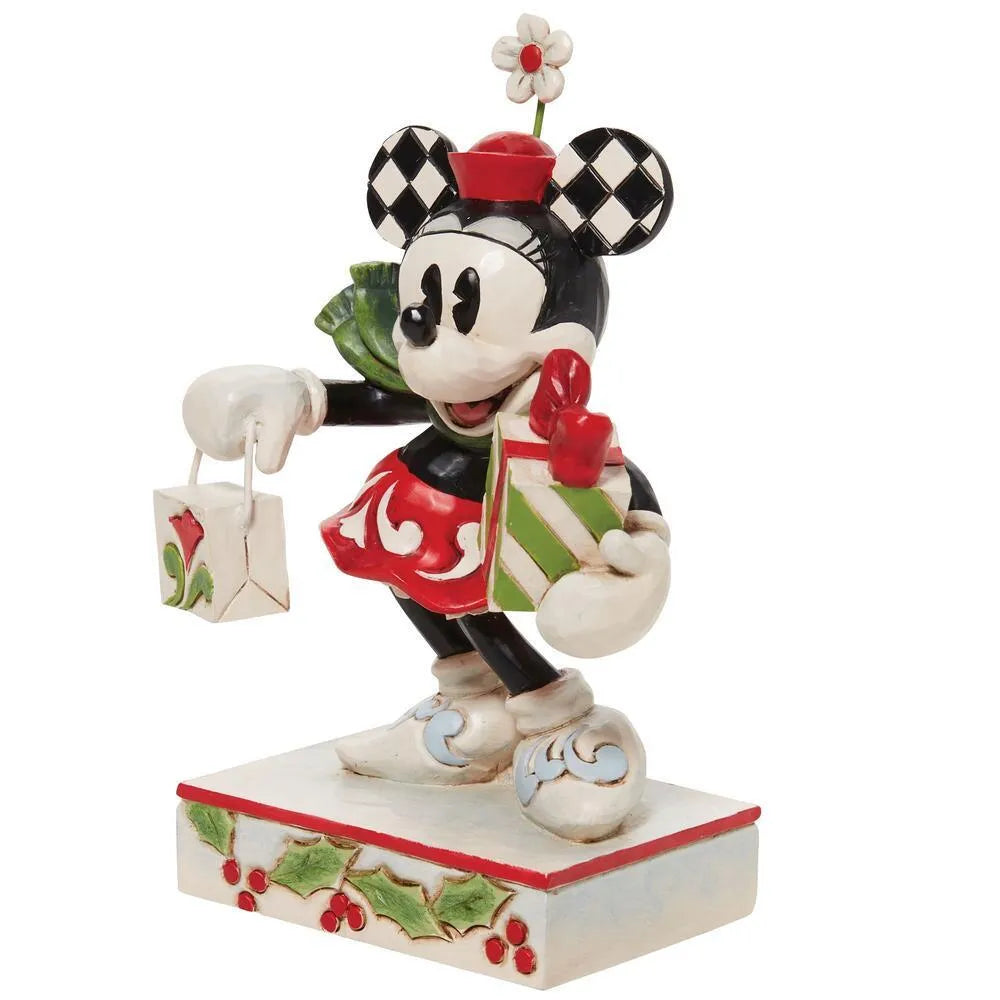 Three-quarter view of Minnie Mouse figurine in red scrollwork dress, checkered ears, carrying striped gift and shopping bag, holly base 