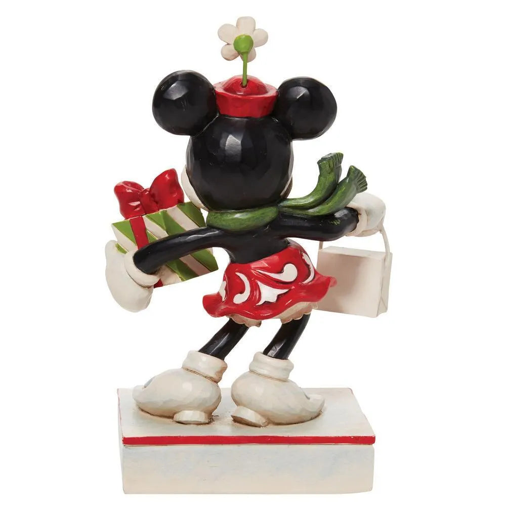 Rear view of Minnie Mouse figurine in red scrollwork dress, green scarf, holding a striped gift and shopping bag, holly base