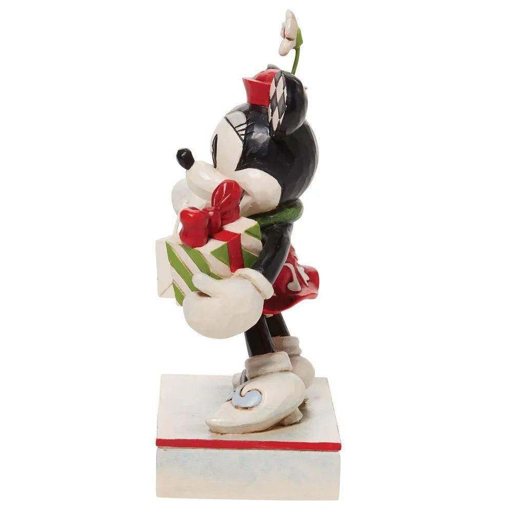 Opposite side view of Minnie Mouse figurine in red dress and green scarf, carrying a gift and decorated shopping bag, holly base