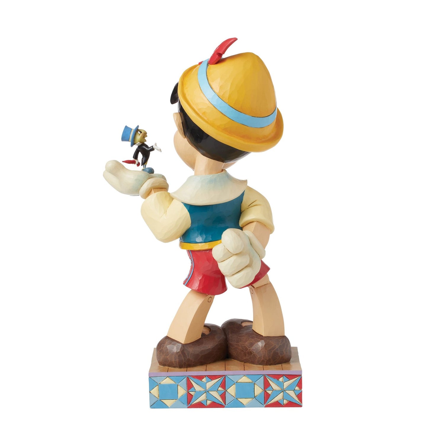 Rear view of Pinocchio figurine holding Jiminy Cricket aloft, yellow hat, blue waistcoat, red shorts, star quilt patterned base