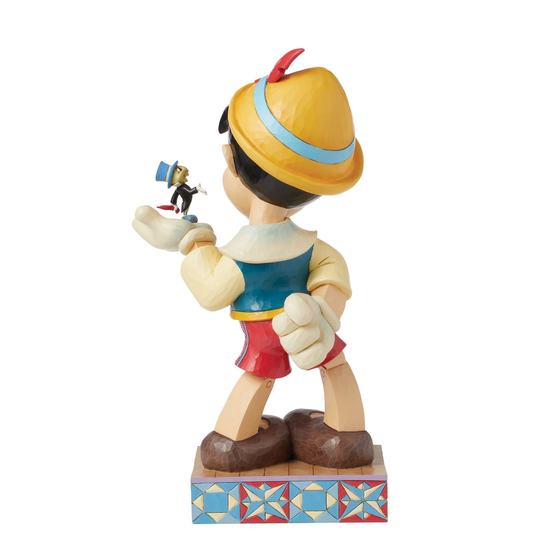 Rear view of Pinocchio figurine holding Jiminy Cricket aloft, yellow hat, blue waistcoat, red shorts, star quilt patterned base