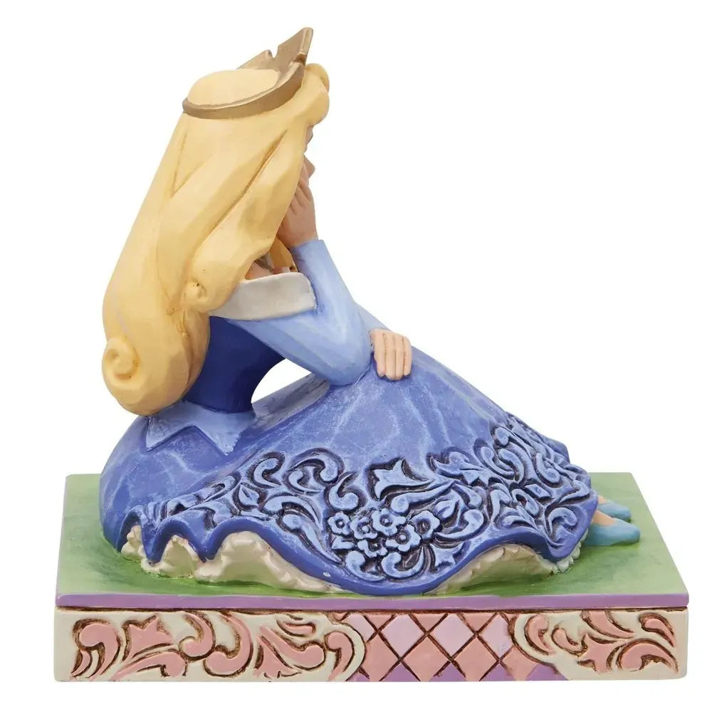 Left side view of Aurora figurine in blue gown with floral scrollwork skirt, gold crown, pink lattice base