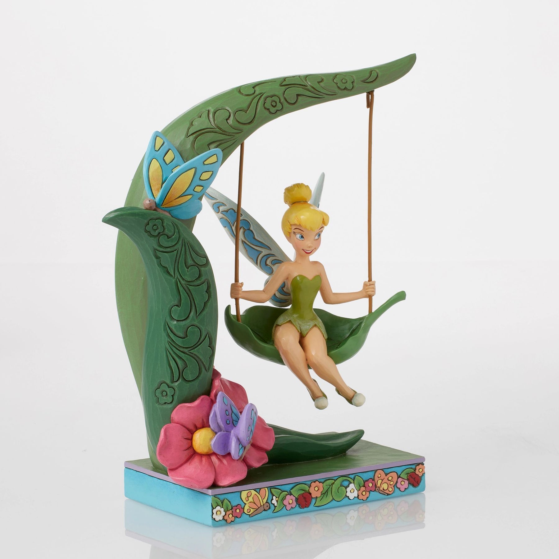 Front view of Tinker Bell figurine on a leaf swing, curved scrollwork stem, blue butterfly, floral painted base 