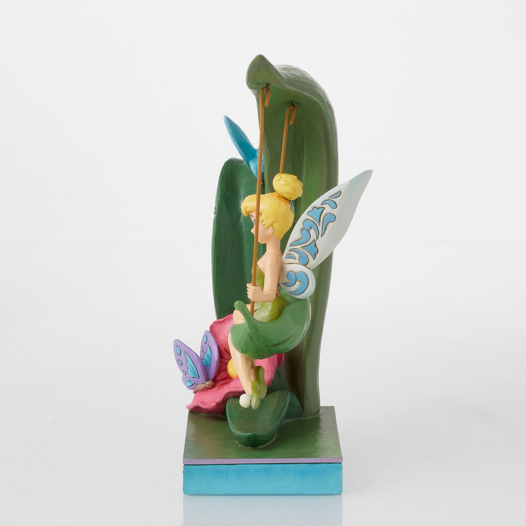 Side view of Tinker Bell figurine seated on leaf swing, detailed wings, pink flower and purple butterfly at base