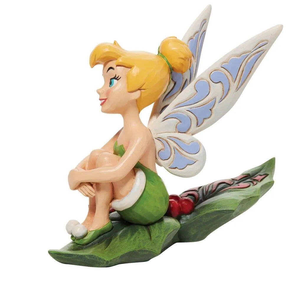 Side view of Tinker Bell figurine seated with knees up on a holly leaf base, scrollwork wings, mistletoe hair detail 