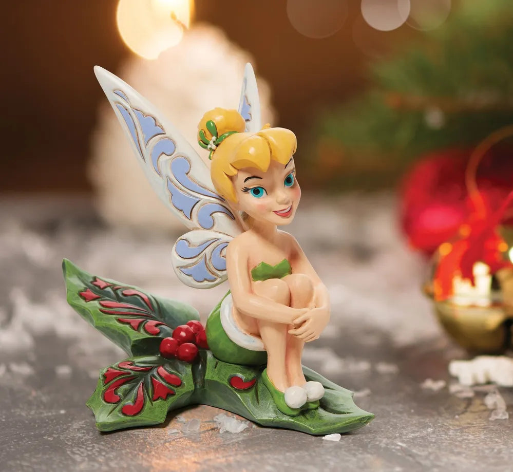 Tinker Bell figurine seated on a holly leaf base with red berries, styled in a Christmas vignette with candle and ornaments
