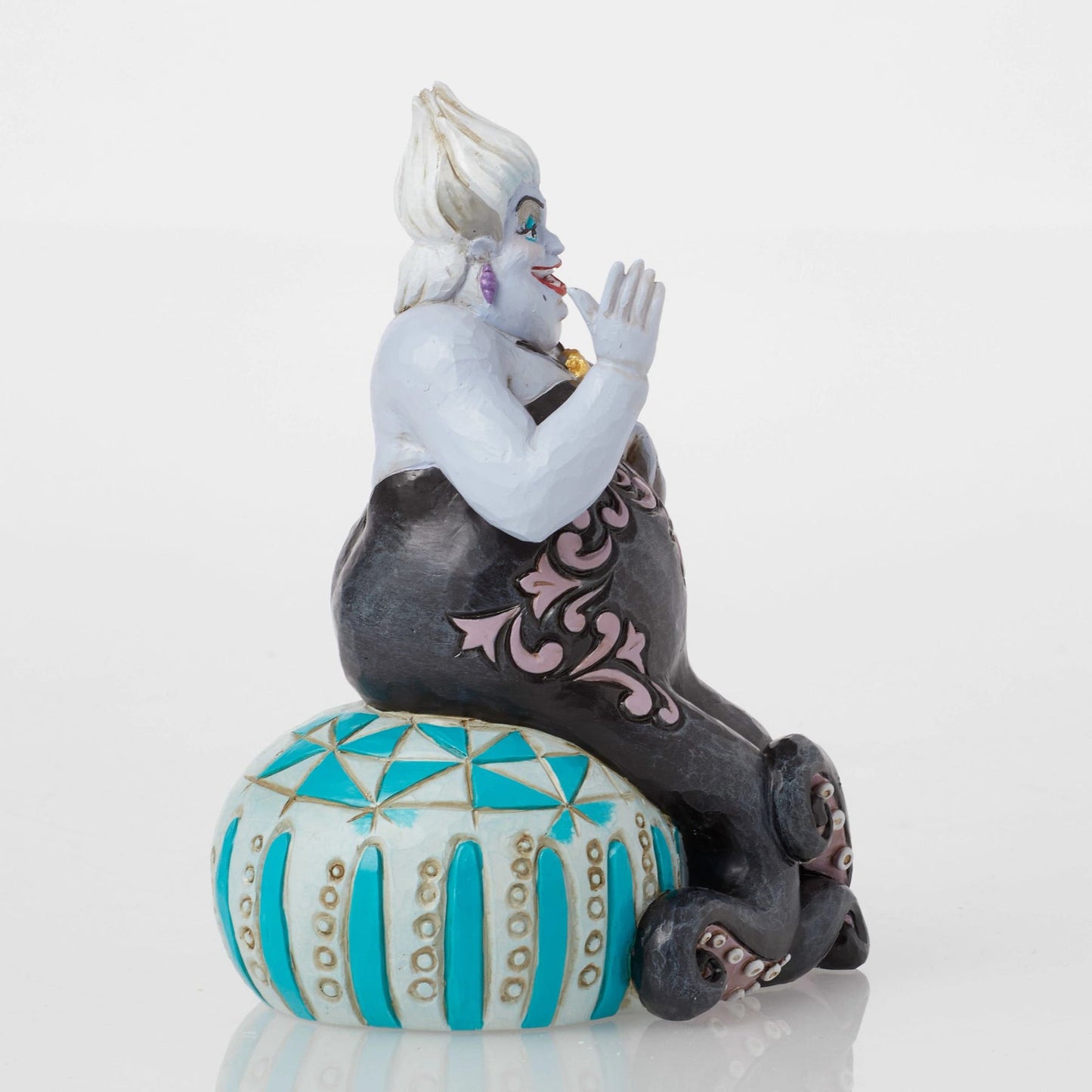 Side view of Ursula figurine with raised hand, black octopus tentacles with pink scrollwork detail, teal base