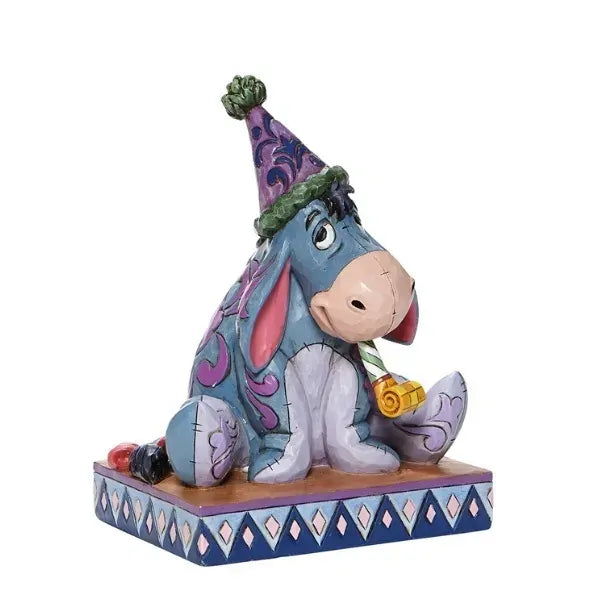 Side view of Eeyore figurine wearing a purple party hat and holding a blower, seated on diamond-patterned base
