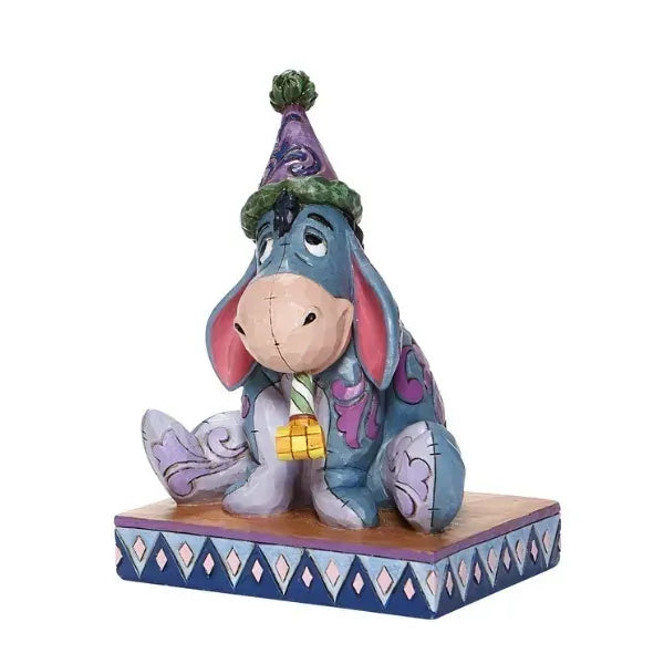 Eeyore figurine front view, wearing a purple party hat with a party blower, seated on a diamond-patterned base