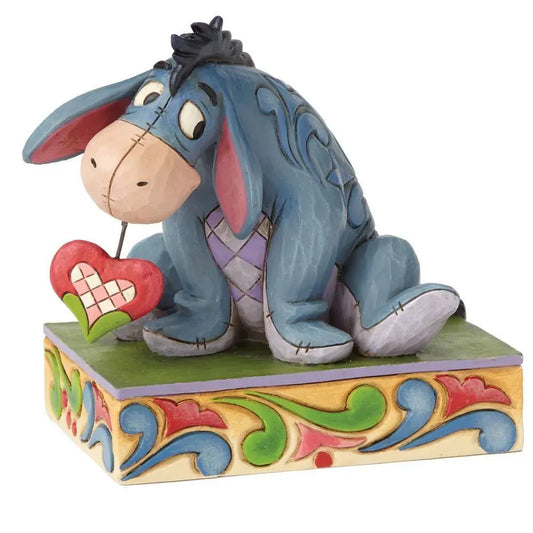 Eeyore from Winnie the Pooh figurine front view, seated with drooping ears beside a small red heart on a scrollwork base