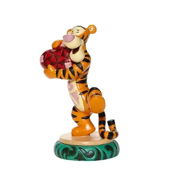 Side view of Tigger figurine clutching a red heart to his chest, one leg raised, on green decorated round base
