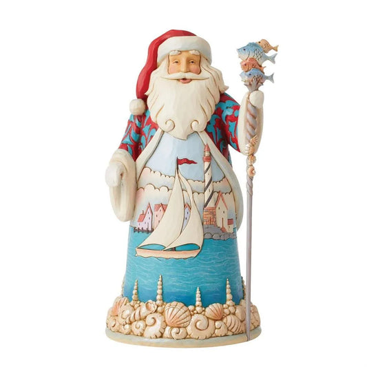 Front view of a coastal Santa figurine; robe features a sailboat and lighthouse scene, fish-topped staff, seashell-decorated base
