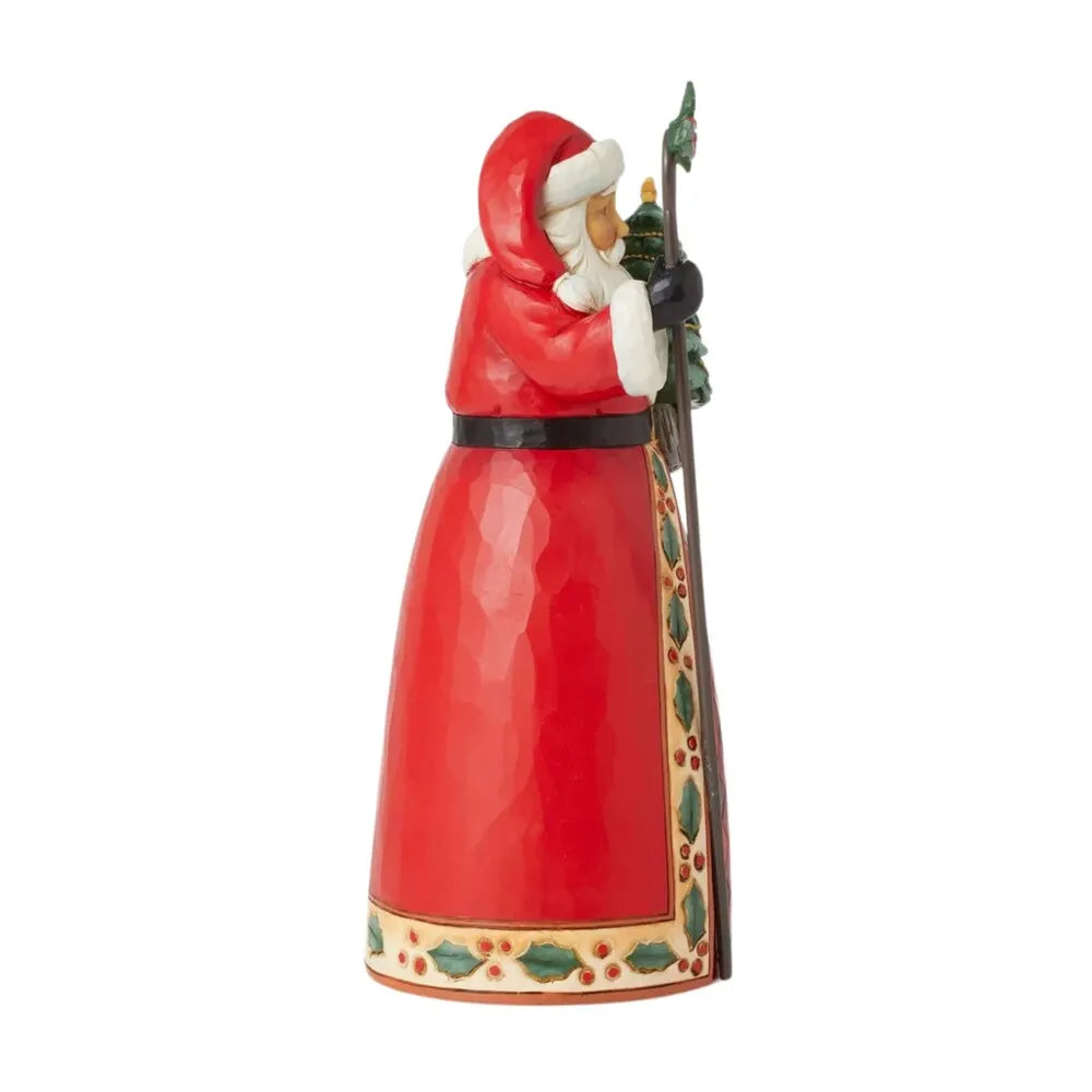 Side view of Santa figurine in red coat with plaid and holly border, carrying a decorated Christmas tree and holly-topped staff 