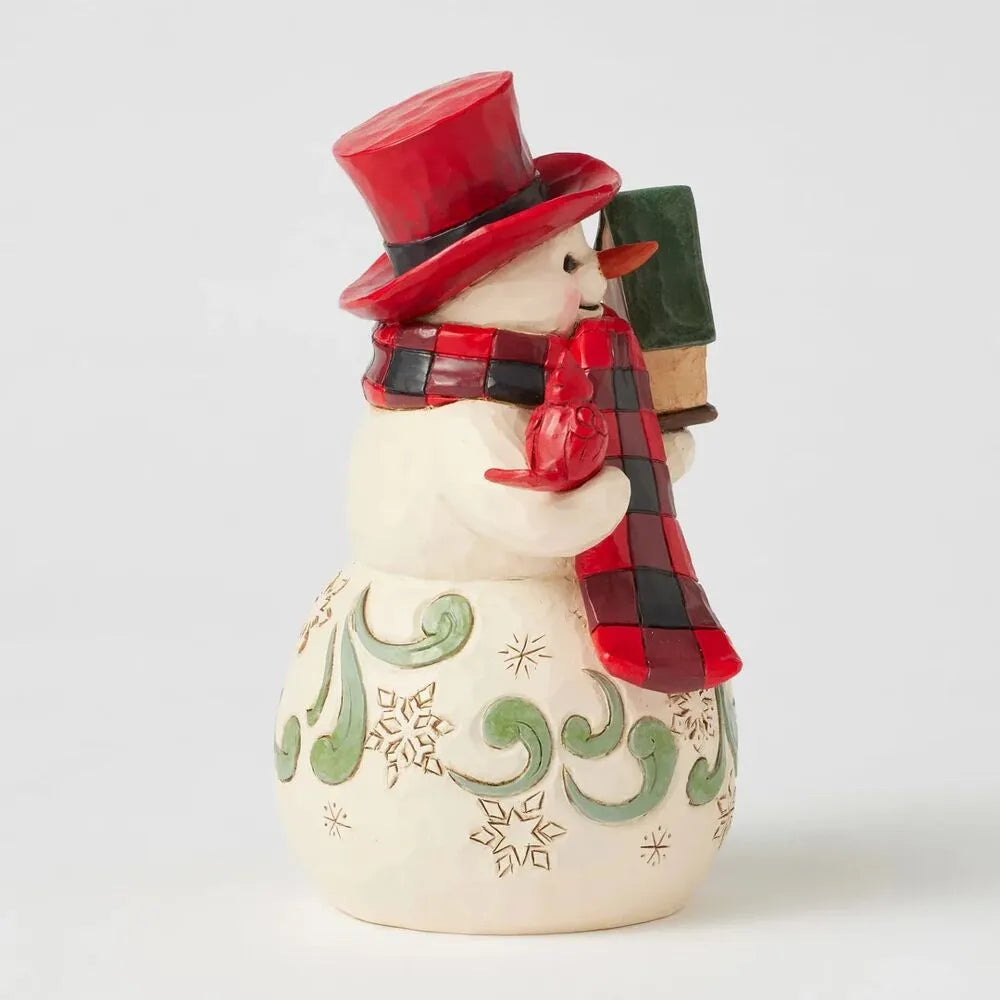 Side view of a Jim Shore snowman figurine in a red top hat and buffalo check scarf, holding a birdhouse, with snowflake body detail