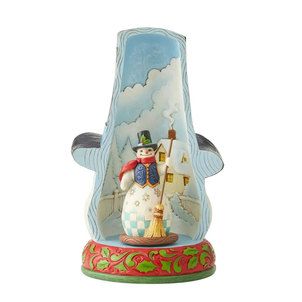 Rear view of a snowman top hat figurine; interior reveals a small snowman figure before a snowy village scene, holly base