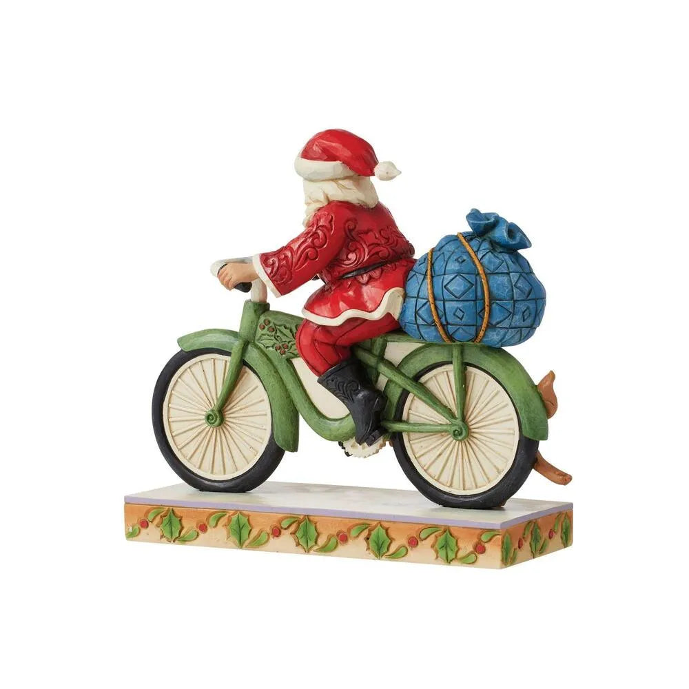 Rear three-quarter view of Santa figurine on green bicycle with blue patterned gift sack tied on back, holly-decorated base