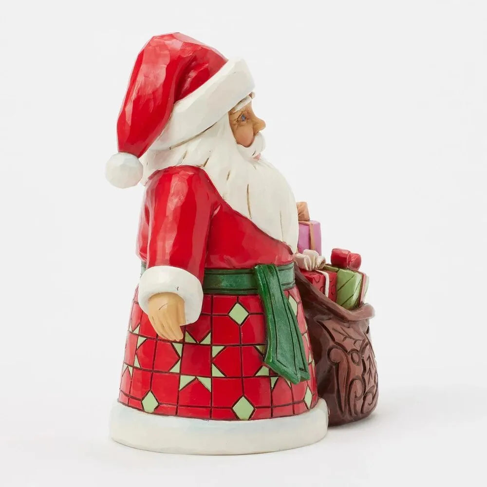 Side view of Santa figurine with geometric patterned robe beside a gift-filled sack with scrollwork detail, green sash at waist