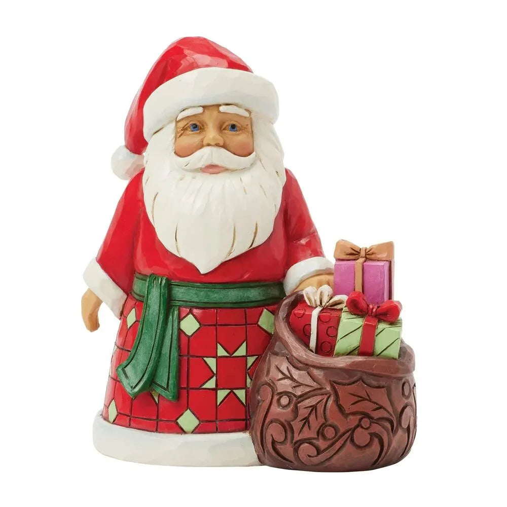 Front view of Santa figurine in red and green geometric patterned robe, standing beside a scrollwork sack overflowing with wrapped gifts