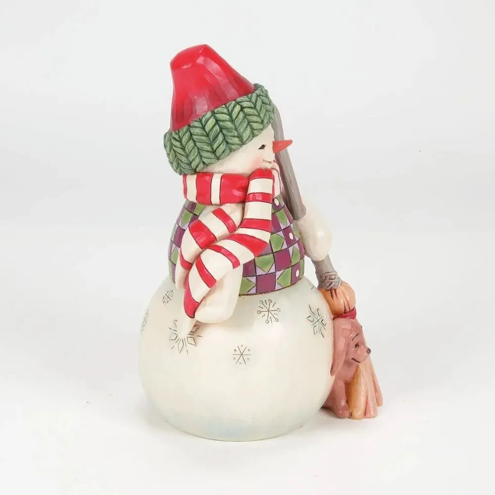 Side view of a Jim Shore snowman figurine holding a broom, with a small dog nestled at the base beside the bristles