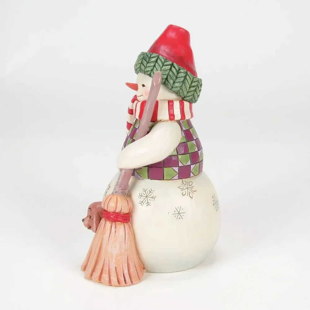 Angled side view of a Jim Shore snowman figurine with striped scarf and snowflake-detailed body, small dog beside the broom