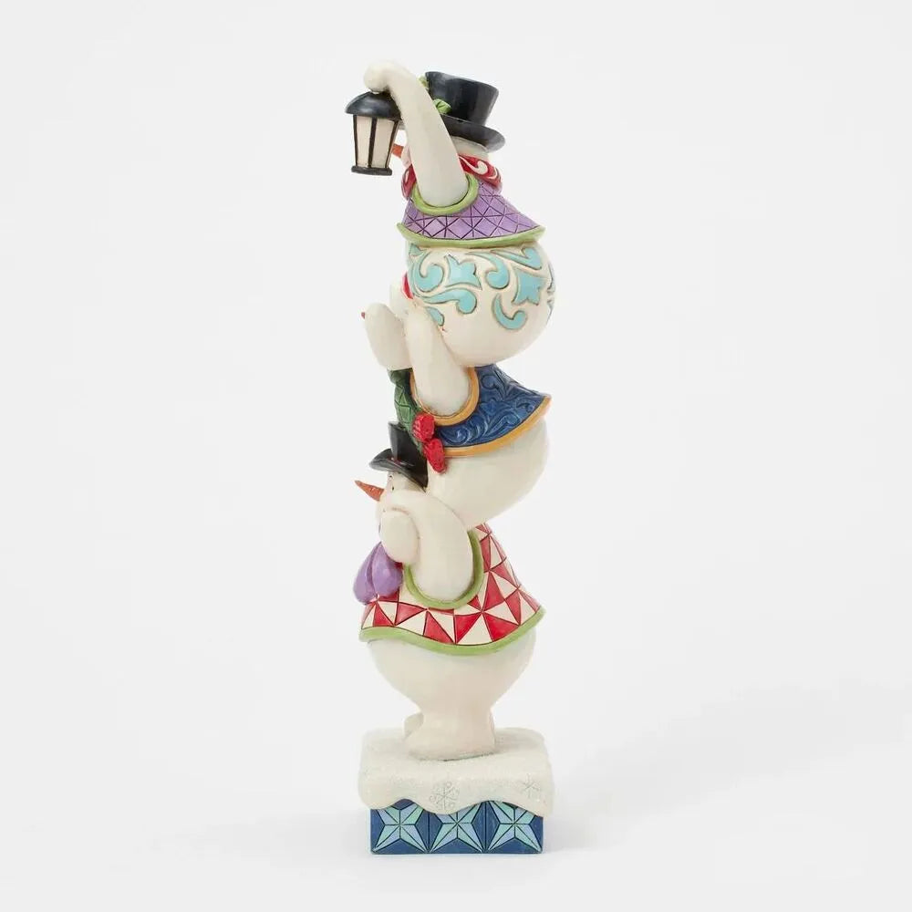 Side view of a Jim Shore triple stacked snowman figurine, the top snowman holding a lantern aloft, on a geometric snowflake base
