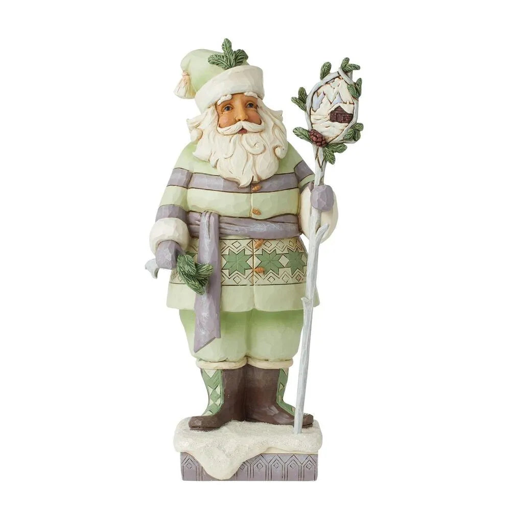 Front view of Santa figurine in sage green Nordic coat, holding a staff with a winter cabin scene medallion, snowy base