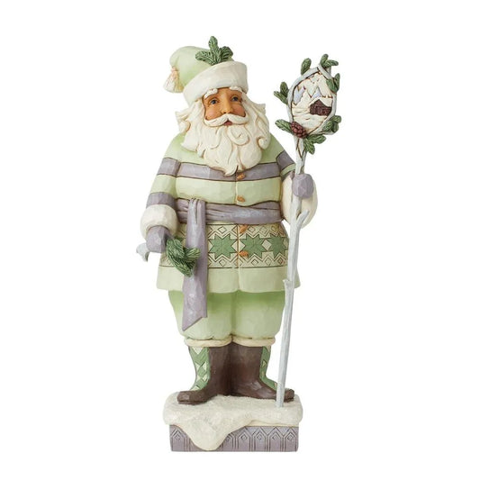 Front view of Santa figurine in sage green Nordic coat, holding a staff with a winter cabin scene medallion, snowy base