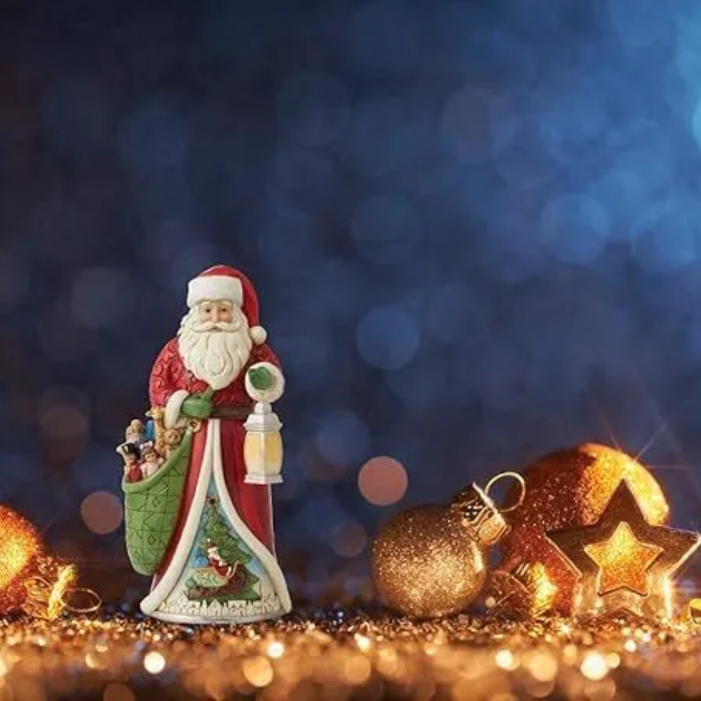 Santa figurine with toy sack and lantern displayed among gold Christmas ornaments and stars against a bokeh blue background