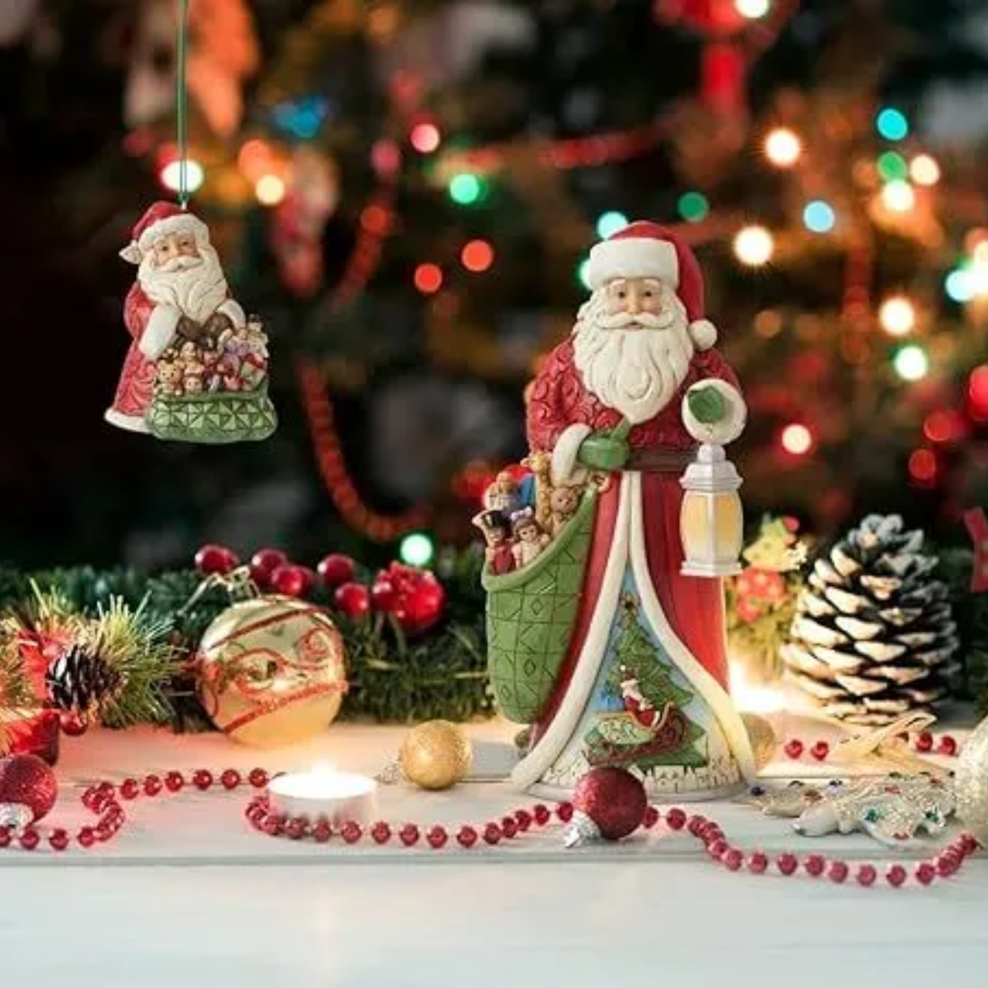 Santa figurine with toy sack and lantern styled in a Christmas vignette with ornaments, pine, candle and a lit tree backdrop 