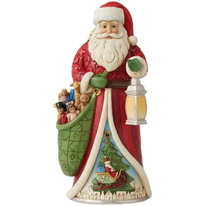 Santa figurine in red scrollwork coat holding a lantern and toy-filled green sack, robe base features a Christmas tree scene