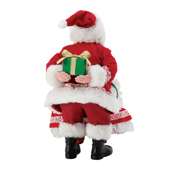 Rear view of Santa Claus figurine holding a wrapped gift with gold ribbon, dressed in a red suit
