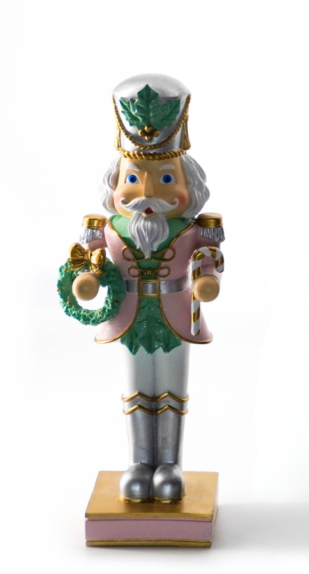 Pastel nutcracker figurine holding a green wreath with gold bow, dressed in pink, green, and gold uniform