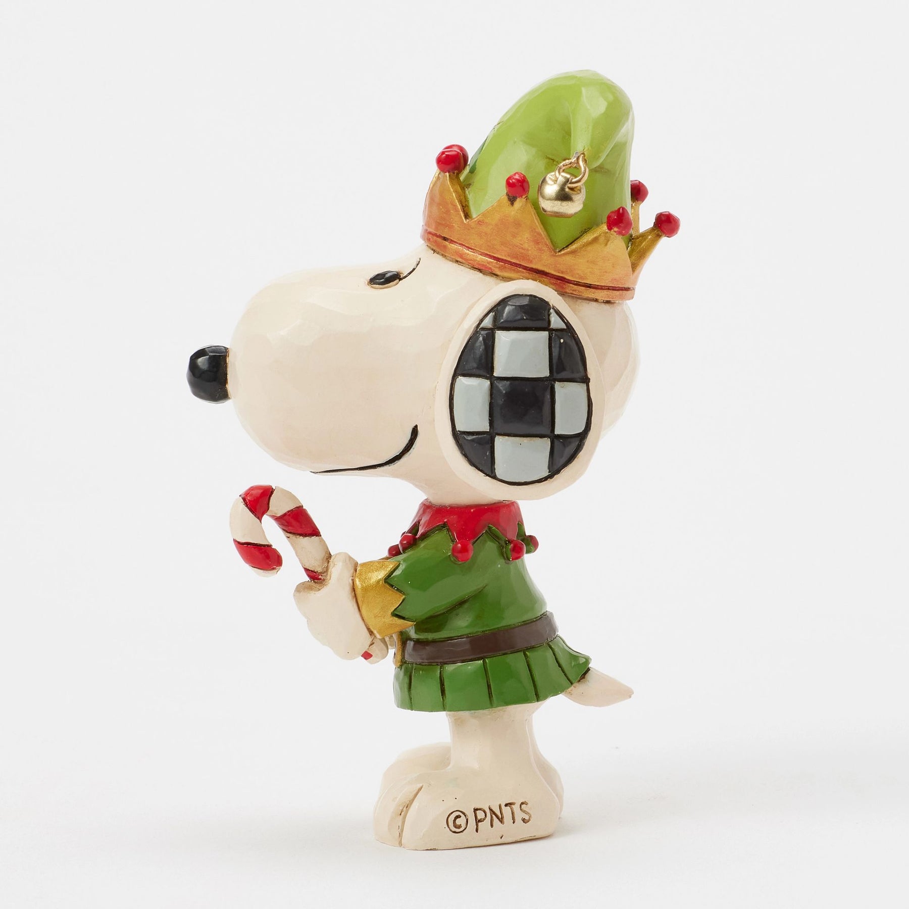Right profile, eye-level angle Snoopy elf figurine facing right, wearing green jester hat with gold bell and red berries, holding candy cane, checkered ear detail