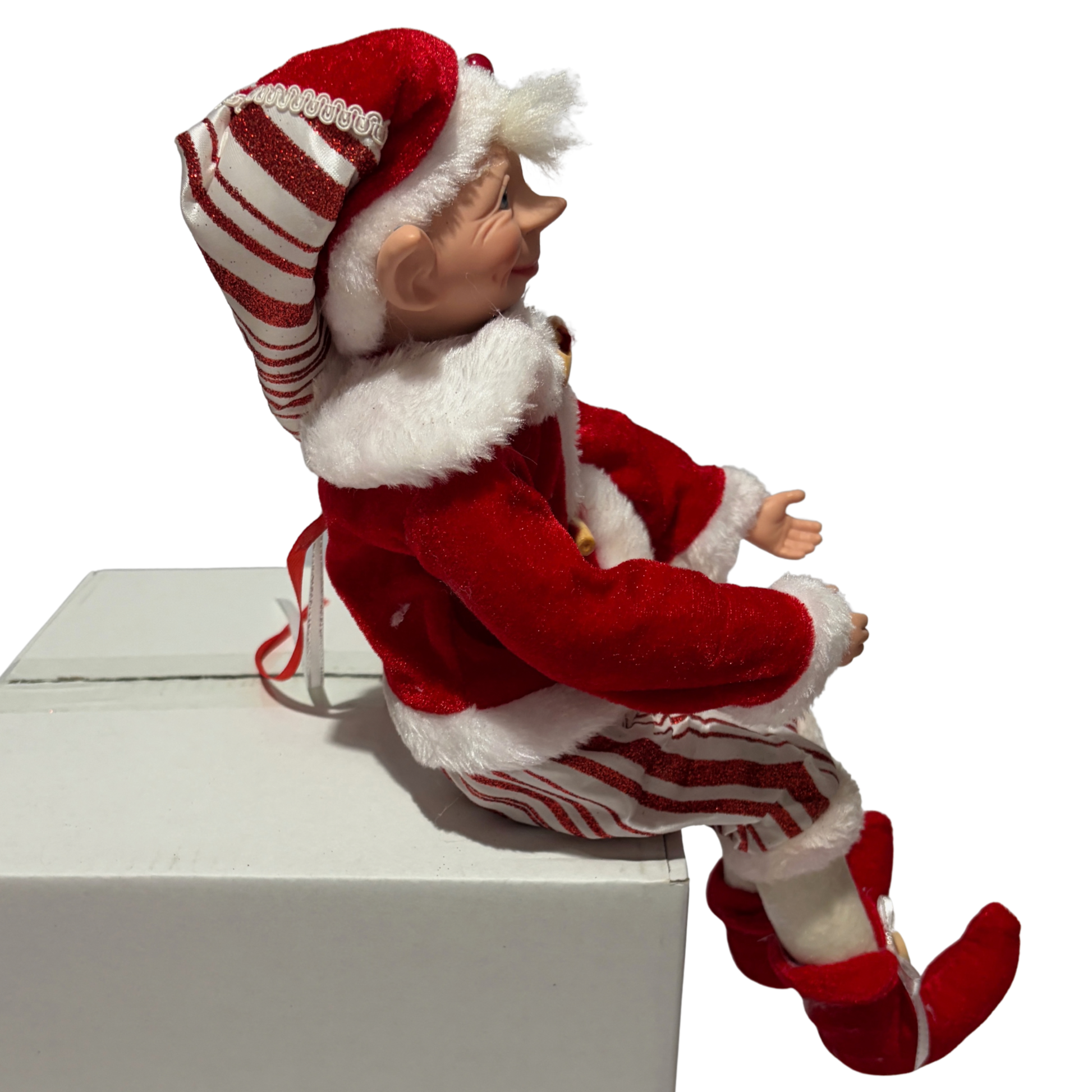 Sitting Christmas elf in red velvet jacket with white fur trim and striped trousers
