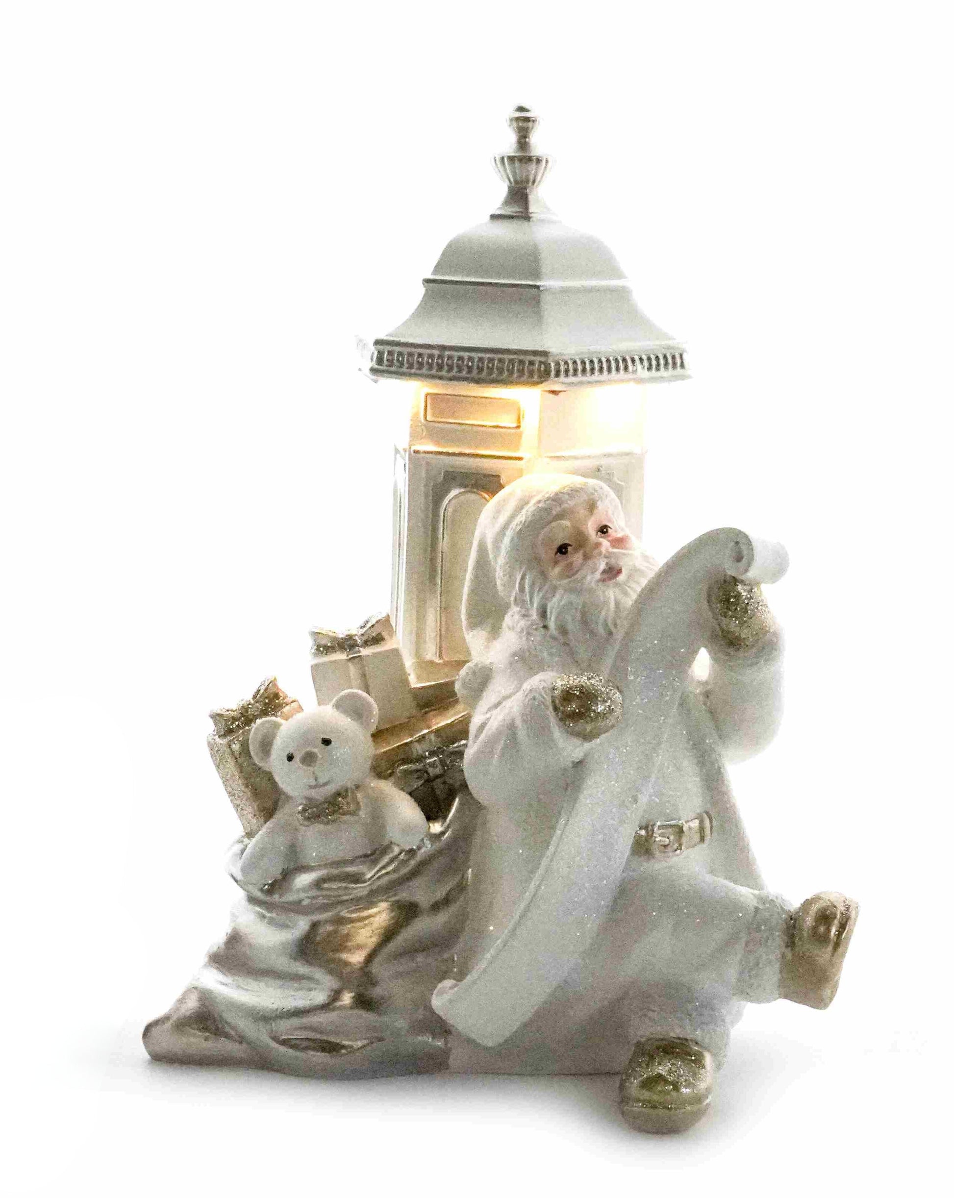 White and gold Santa figurine checking his list beside a glowing postbox with a sack of gifts and teddy bear