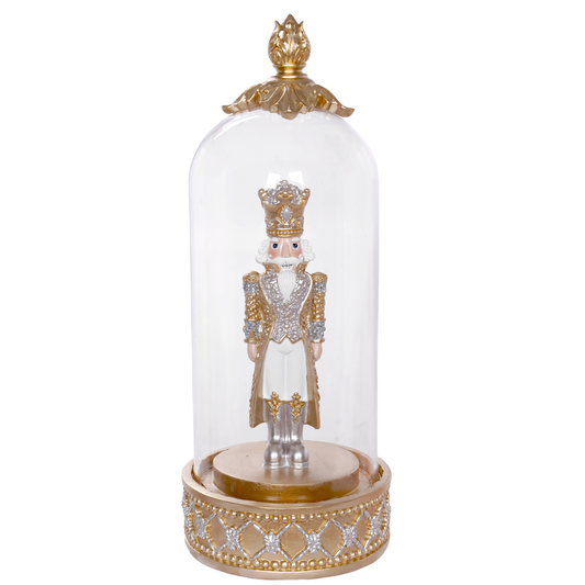 Silver and gold nutcracker figurine in decorative coat and gold crown, housed in a glass dome on a lattice base