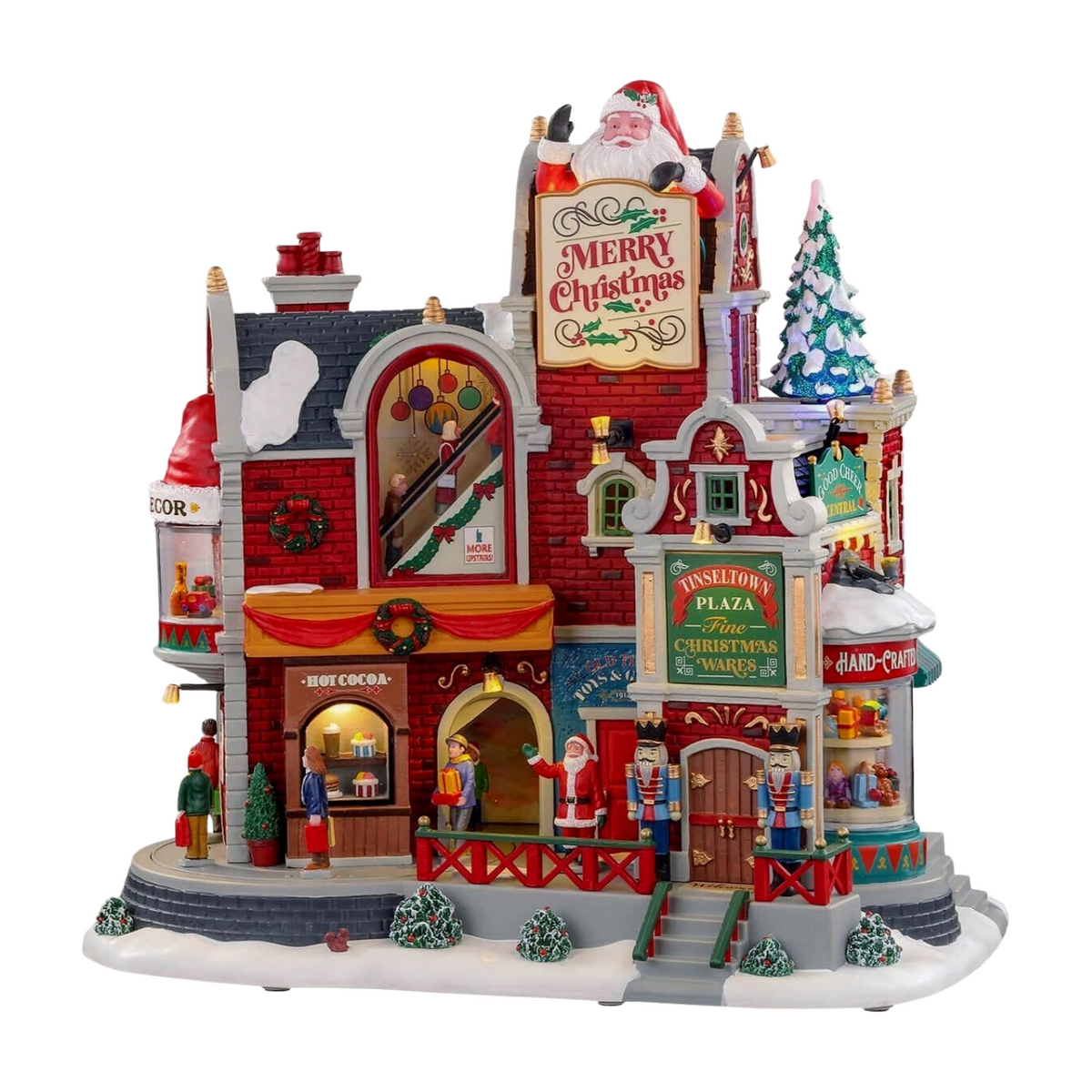 Illuminated Christmas village building with Santa figure, Tinseltown Plaza shops, nutcrackers, hot cocoa stand, and decorated tree 